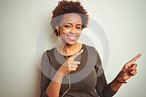 African american woman wearing earphones listening to music over isolated background smiling and looking at the camera pointing