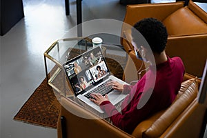 African american woman wearing face mask having video call with diverse colleagues displayed on lapt