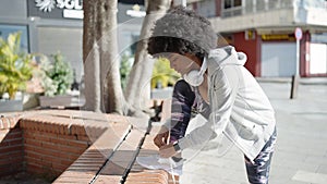 African american woman wearing headphones tying shoes at park