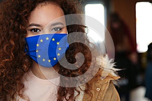 African American woman wearing medical mask with European Union flag, outdoors. Coronavirus outbreak in Europe