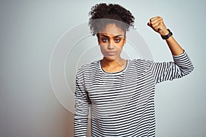 African american woman wearing navy striped t-shirt standing over isolated white background Strong person showing arm muscle,