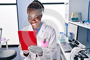 African american woman wearing scientist uniform using touchpad at laboratory