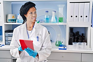 African american woman wearing scientist uniform using touchpad at laboratory