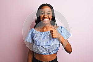 African american woman wearing striped t-shirt standing over isolated pink background doing happy thumbs up gesture with hand