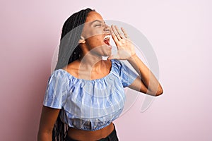 African american woman wearing striped t-shirt standing over  pink background shouting and screaming loud to side with