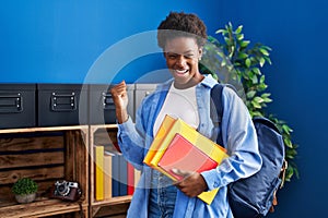 African american woman wearing student backpack and holding books screaming proud, celebrating victory and success very excited