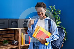 African american woman wearing student backpack and holding books smiling happy and positive, thumb up doing excellent and