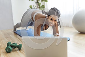 African american woman working out abdo in home livingroom gym with laptop