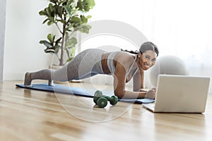 African american woman working out abdo in home livingroom gym with laptop