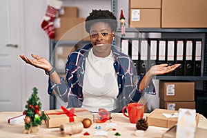 African american woman working at small business doing christmas decoration clueless and confused expression with arms and hands