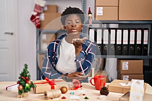 African american woman working at small business doing christmas decoration looking at the camera blowing a kiss with hand on air