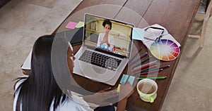 African american woman writing on memo notes having a video call on laptop at home