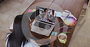 African american woman writing on memo notes having a video call on laptop at home