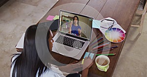 African american woman writing on memo notes while having a video call on laptop at home