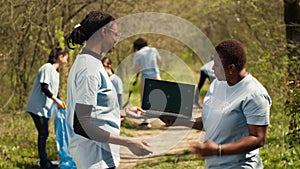 African american women use laptop with greenscreen during litter cleanup