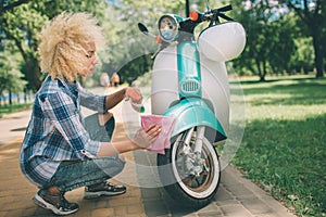 African American women washing motor scooter. Girl cleaning a the blue moped or motorcycle