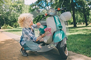 African American women washing motor scooter. Girl cleaning a the blue moped or motorcycle