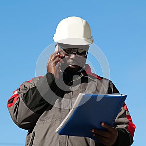 African american worker looks in work papers and talks on smartphone