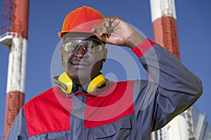 African American Worker In Protective Workwear Standing In Front Of Industrial Chimneys