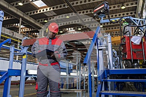 African American Worker In Protective Workwear Writing On Clipboard In Industrial Interior