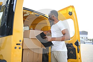 african american Worker unloading boxes from van outdoors. Moving service concept. Male employee of moving company makes