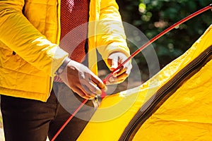 African american in yellow jacker putting on a tent in forest