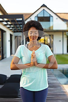 African american young afro woman with hands clasped and eyes closed exercising in backyard