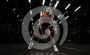 African-american young basketball player in action and motion in flashlights over dark gym background. Concept of