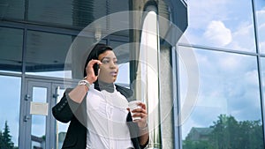 African american young business woman in suit and white shirt is talking on phone outside near modern office building