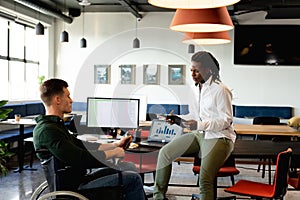 African american young businessman discussing with caucasian colleague sitting in wheelchair