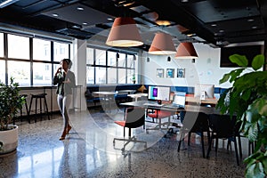 African american young businesswoman talking on mobile phone while walking in creative office