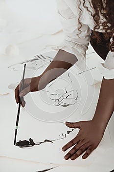 African-american young curly woman painting with black color ink on white floor