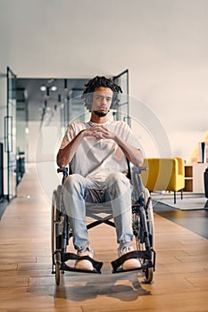 An African-American young entrepreneur in a wheelchair is surrounded by his business colleagues in a modern office