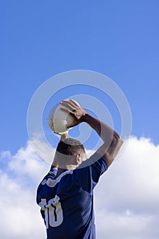 African American young male athlete holding a rugby ball, ready to throw, copy space