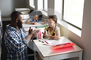 African american young male teacher communicating in sign language with caucasian elementary girl