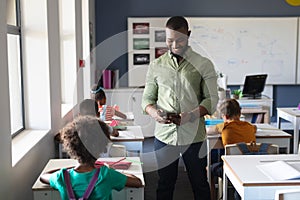 African american young male teacher using digital tablet while standing by multiracial students