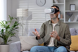 African american young man sitting on sofa at home wearing 3d glasses, wearing virtual reality glasses, playing online