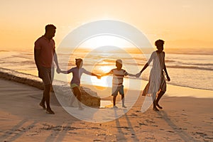 African american young parents holding daughter and son\'s hands while walking at beach against sky