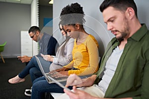 An african american young woman applicant using laptop preparing for employment interview sitting on chairs in queue