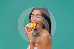 African american young woman biting orange slice on turquoise studio background. The concept of beauty and healthy