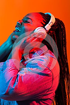 African american young woman listening to music online dancing and singing with headphones, neon light. Music and