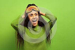 African-american young woman`s portrait in ski mask on green background