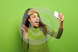 African-american young woman`s portrait in ski mask on green background