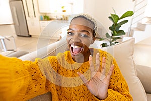 African american young woman with short hair screaming and waving hand while taking selfie on sofa