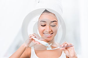 African american young woman with towel wrapped over head putting toothpaste photo
