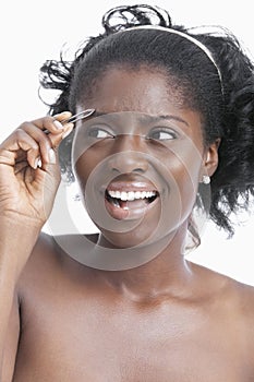 African American young woman tweezing her eyebrows over white background