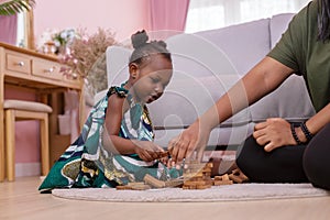 African Americans` mother and daughter playing block wooden games together in living room. black people or African Americans. Hom