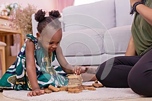 African Americans` mother and daughter playing block wooden games together in living room. black people or African Americans. Hom