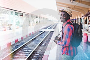 African backpackers wearing hats and cameras waiting for a train at a station to travel.Adventure travel concept