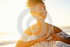 African beautiful girl making hand heart at beach during sunset